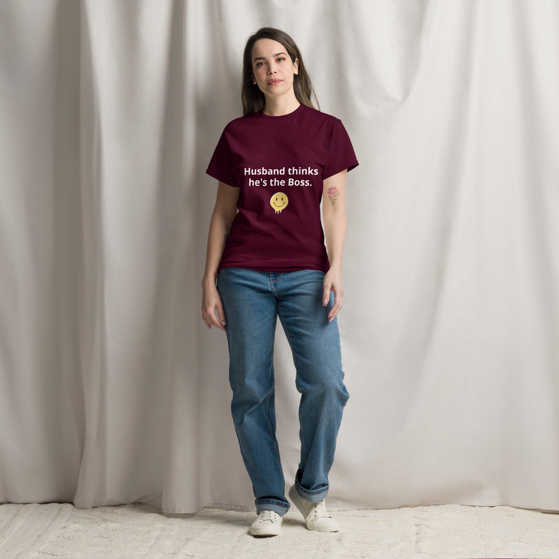 A person standing in a room wearing a maroon t-shirt with the text 'Husband thinks he's the Boss' printed on the front.