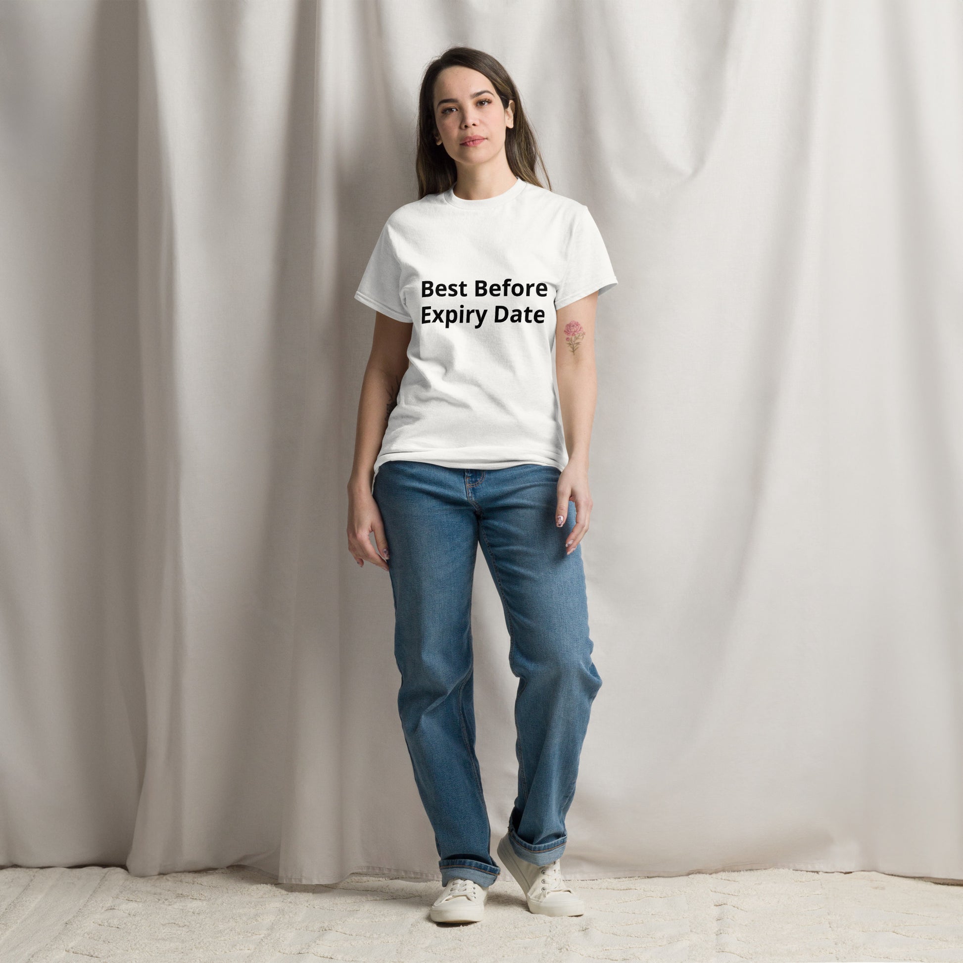 A person standing in a casual pose wearing a white unisex crew neck t-shirt with text on the front, paired with blue jeans and white sneakers.