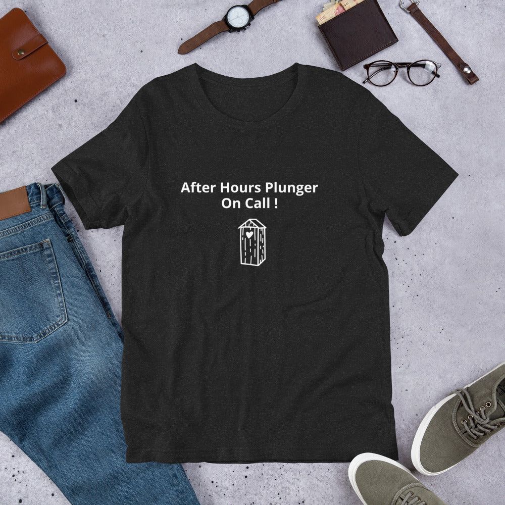 A black t-shirt with the text 'After Hours Plunger On Call!' printed on the front, laid flat with casual clothing items around it.