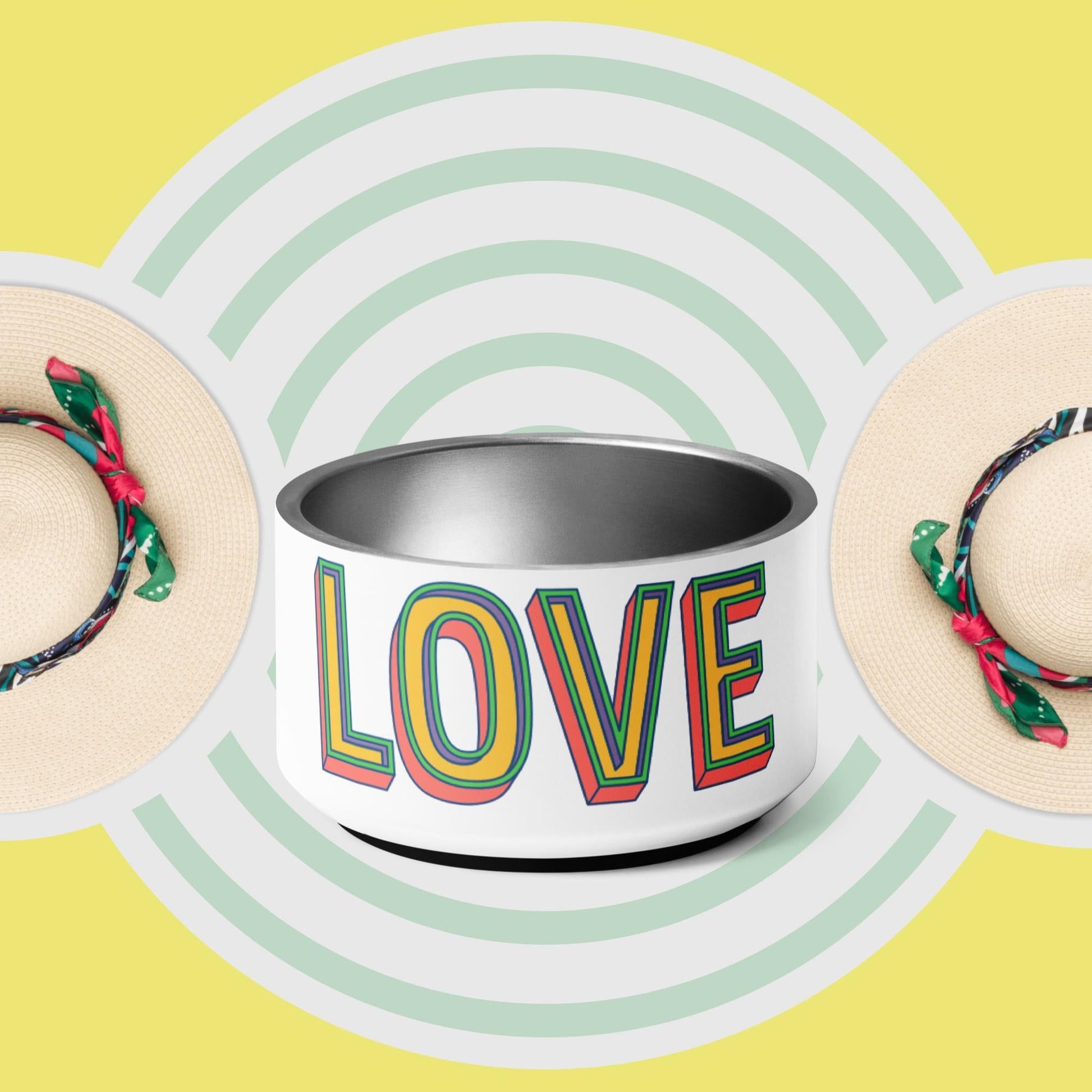 A stainless steel pet bowl with the word 'LOVE' printed on the side, set against a yellow background with a pattern of green concentric circles. The bowl has a double-wall design and anti-slip rubber base.