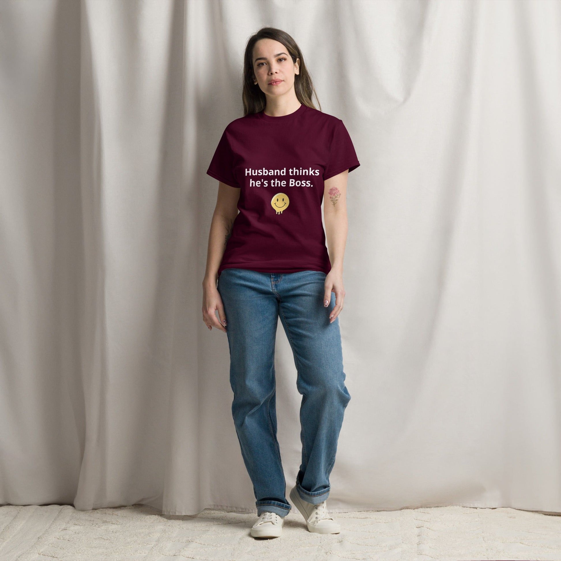 A person standing in a room wearing a maroon t-shirt with the text 'Husband thinks he's the Boss' printed on the front.